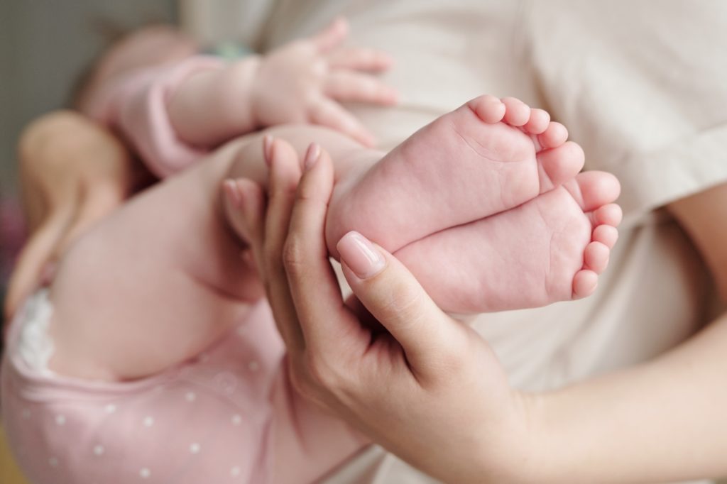 Hand of young woman holding bare feet of her baby daughter